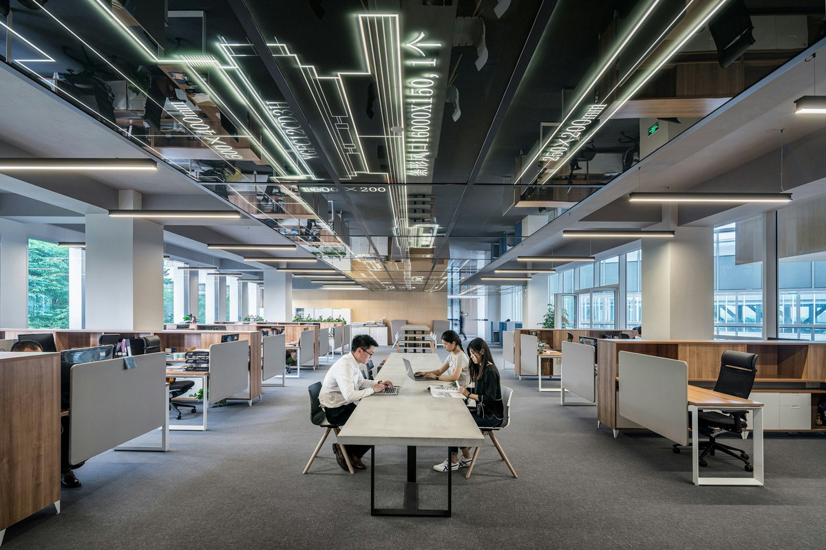 An open-plan engineering office, with three people working at a
                    shared table between rows of desks.
