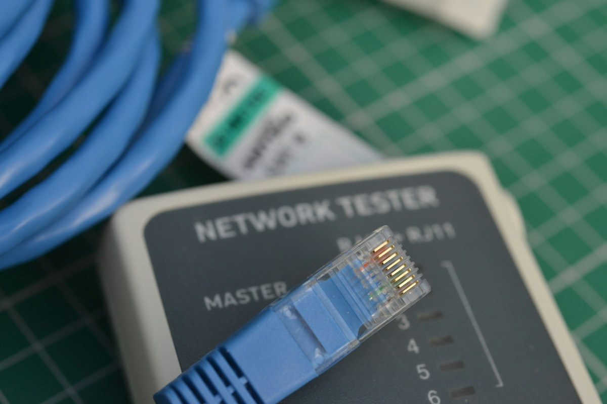 A cable tester on a cutting mat with an RJ45 plug seated in it
                      and a coil of patch cable beside.
