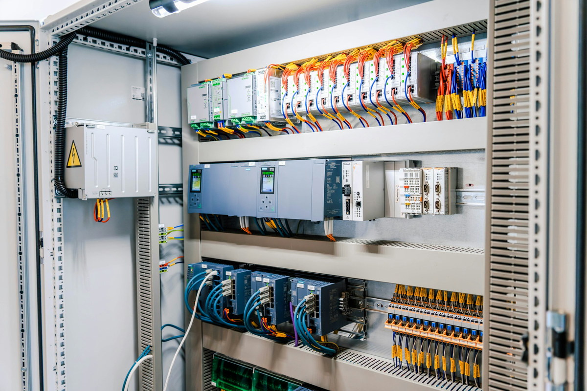An open control cabinet: PLC modules and network switches on DIN rail above rows of numbered terminal blocks.