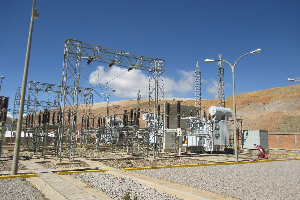 An outdoor substation yard: lattice steel gantries, insulator
                    stacks and a transformer, with a hillside behind.